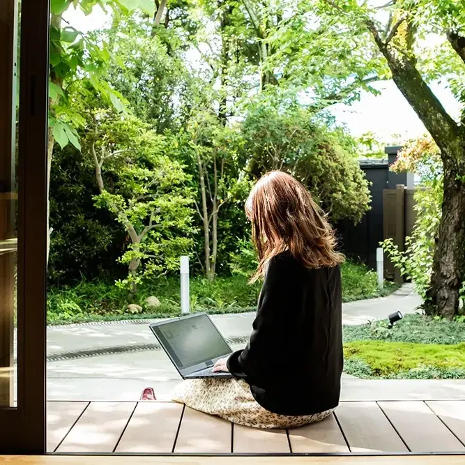 Donna al PC in veranda con giardino rigoglioso